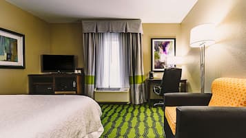A hotel room with a bed, a desk with a chair, a television, and a lamp.