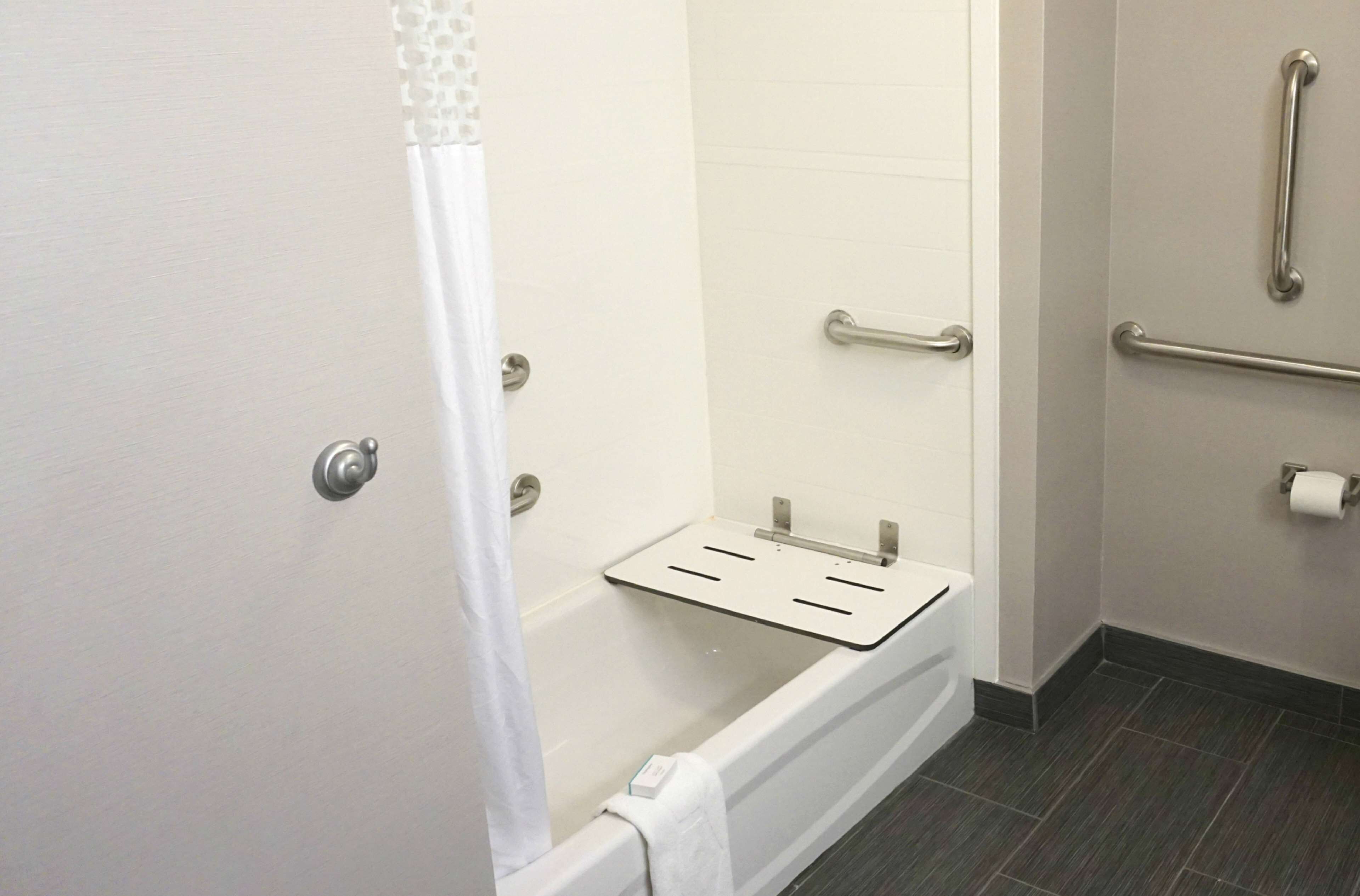 A bathroom with a shower, grab bars, a towel rack, and a toilet paper holder.