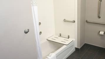 A bathroom with a shower, grab bars, a towel rack, and a toilet paper holder.