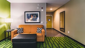 A hotel room with a sofa, a black ottoman, a framed abstract painting, a lamp, and a patterned rug. - Hampton Inn Niagara Falls/Blvd (Niagara Falls)