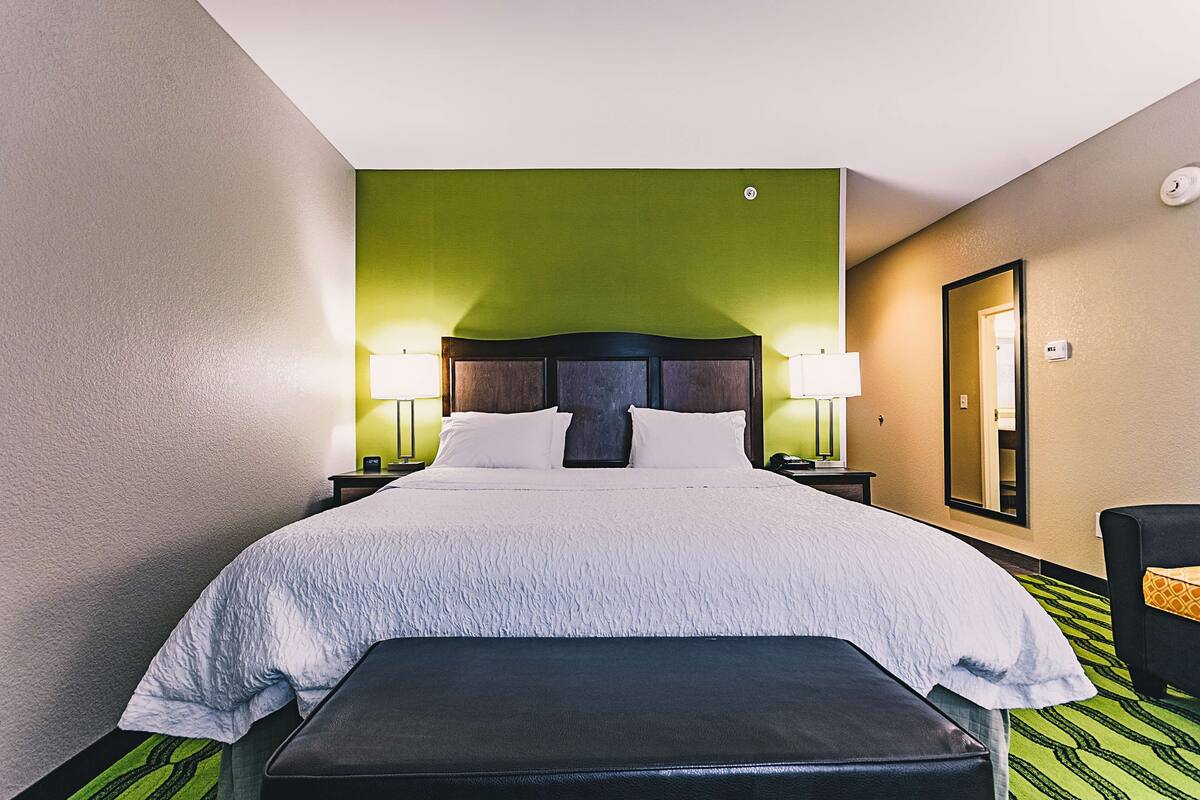 Camera d'albergo con un letto grande, due abat-jour, una panca, uno specchio e un tappeto verde.