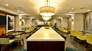 A hotel dining area with a long table, multiple chairs, and a central island. - Hampton Inn Niagara Falls/Blvd (Niagara Falls)