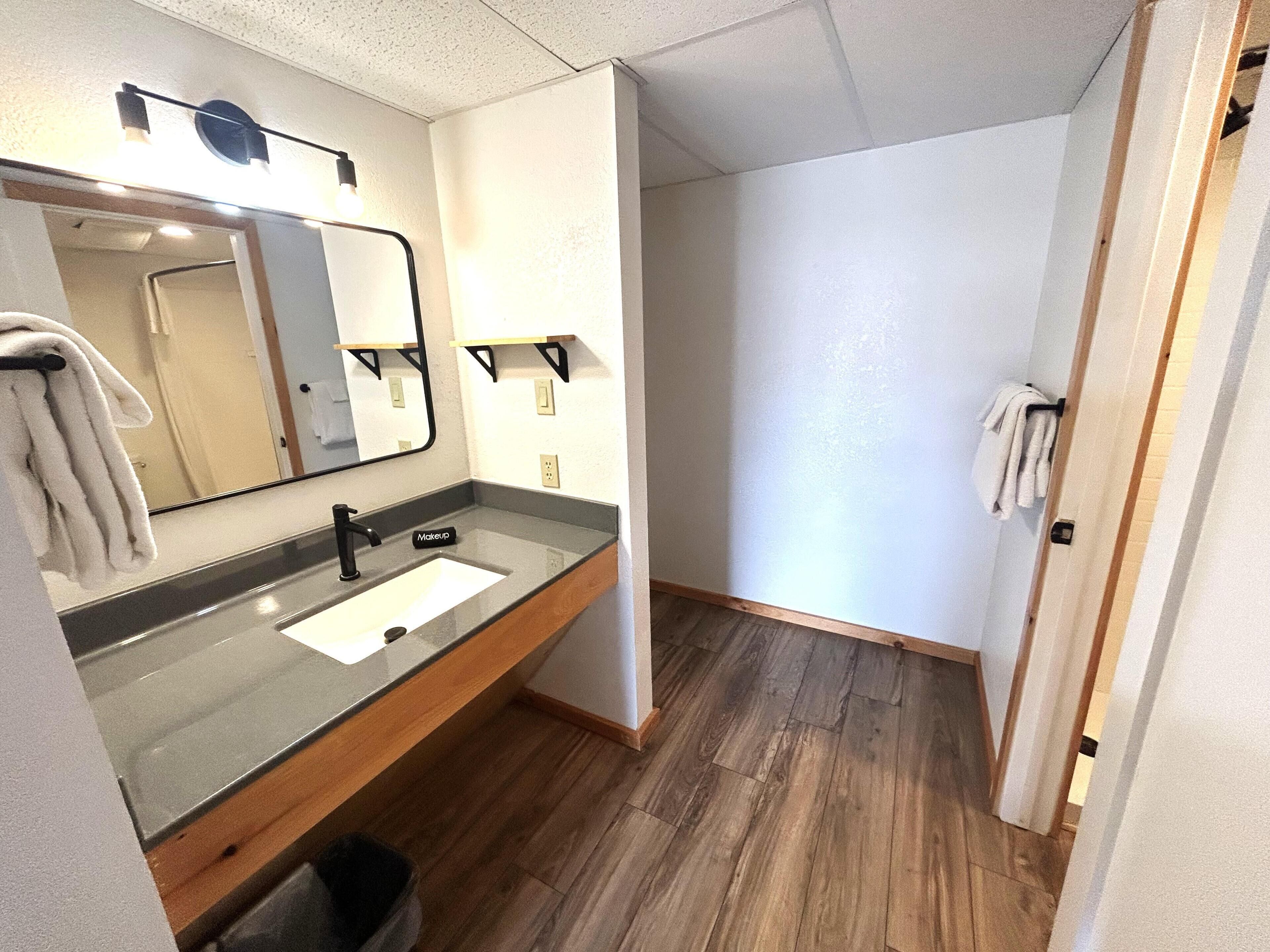 A bathroom with a sink, mirror, towel rack, and wooden flooring.