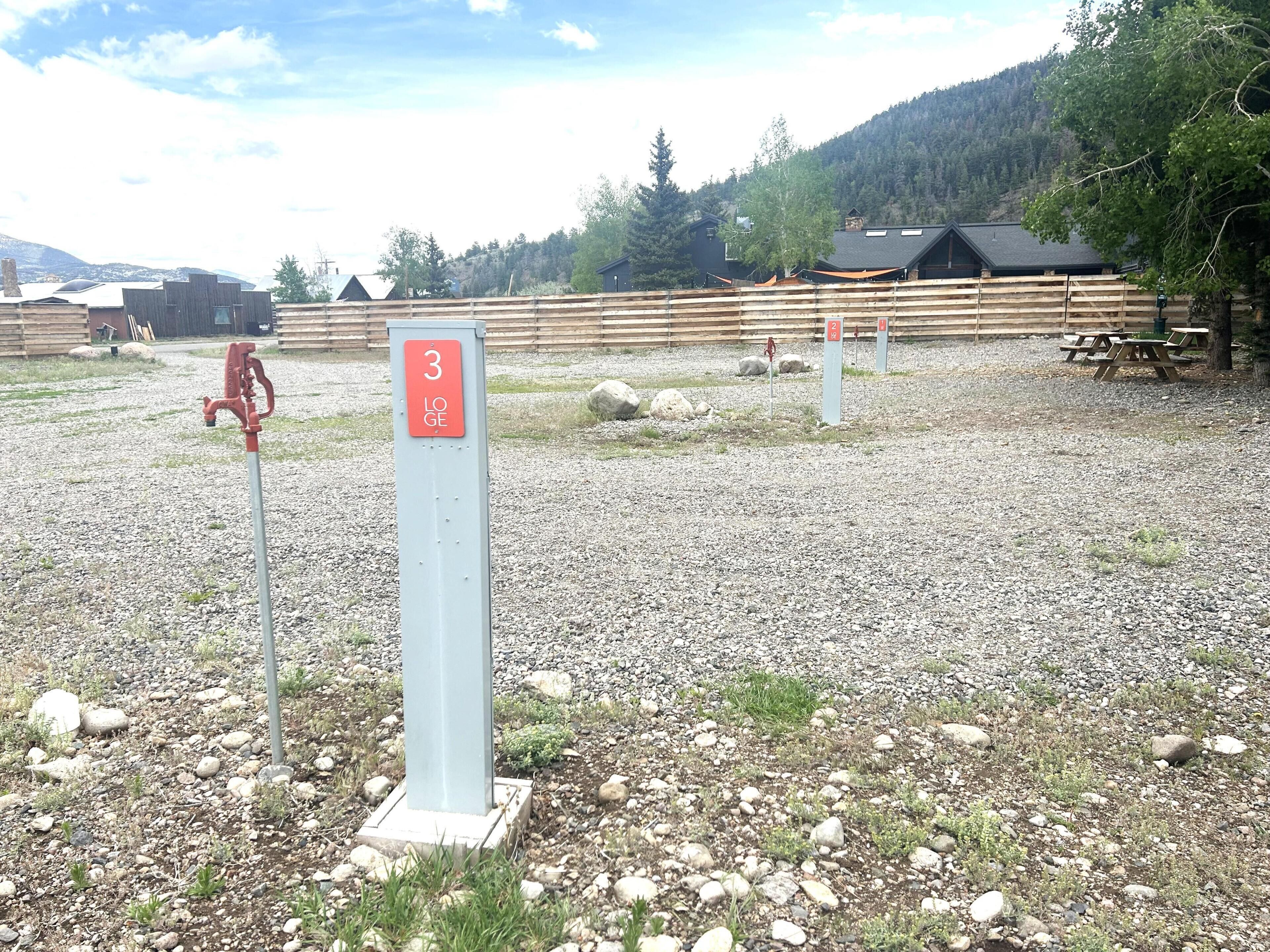 Une zone recouverte de gravier, avec un panneau indicateur numéroté, des clôtures en bois et des tables de pique-nique.