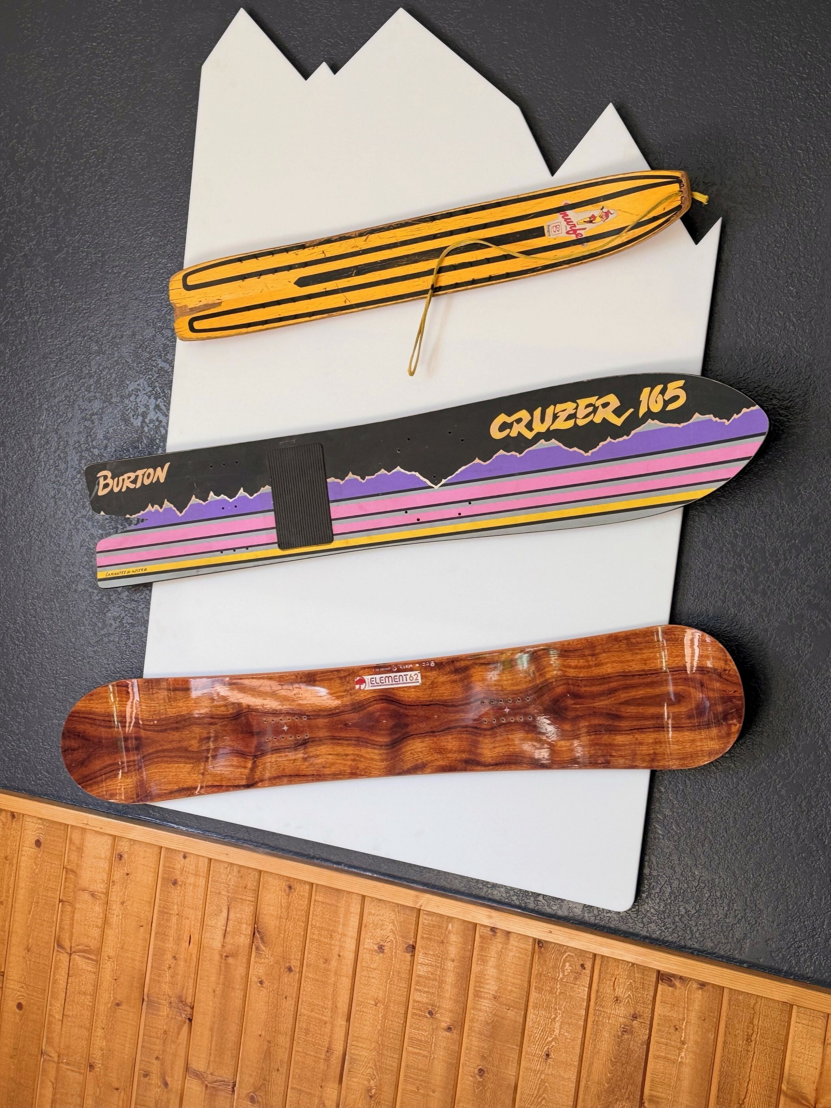 Tres tablas de snowboard con diseños y etiquetas distintas, sobre un mantel blanco sobre un fondo oscuro.