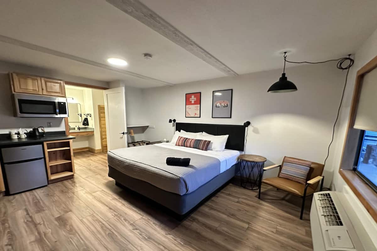 A compact hotel room with a bed, kitchenette, and a small seating area.