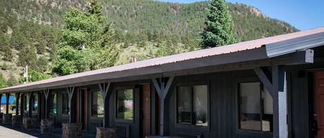 A row of rustic cabins with stone pillars, large windows, and a mountain backdrop.