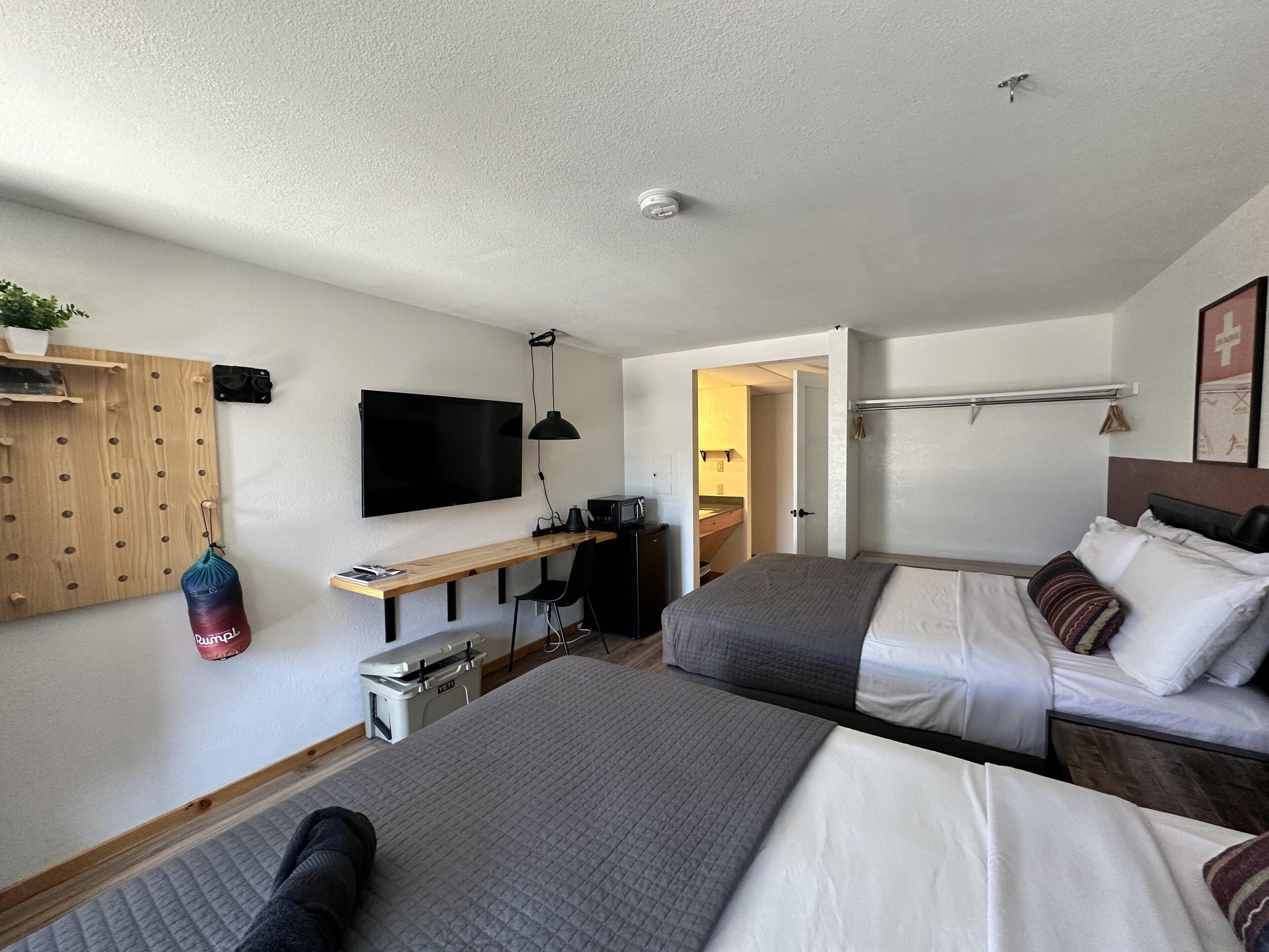 A bedroom with two beds, a desk with a computer, a TV, and a ceiling fan.