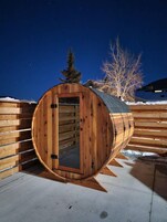Una estructura de madera con forma de barril y una puerta, frente a un paisaje nevado bajo un cielo nocturno despejado.