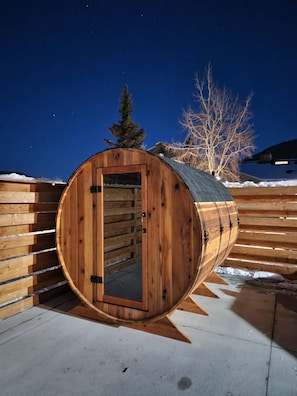 Una estructura de madera con forma de barril y una puerta, frente a un paisaje nevado bajo un cielo nocturno despejado.