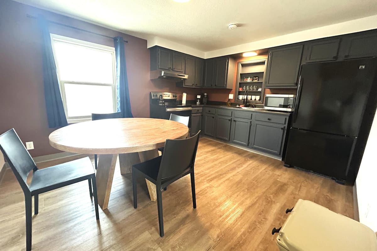 A kitchen with a dining table, chairs, cabinets, a refrigerator, and a window.
