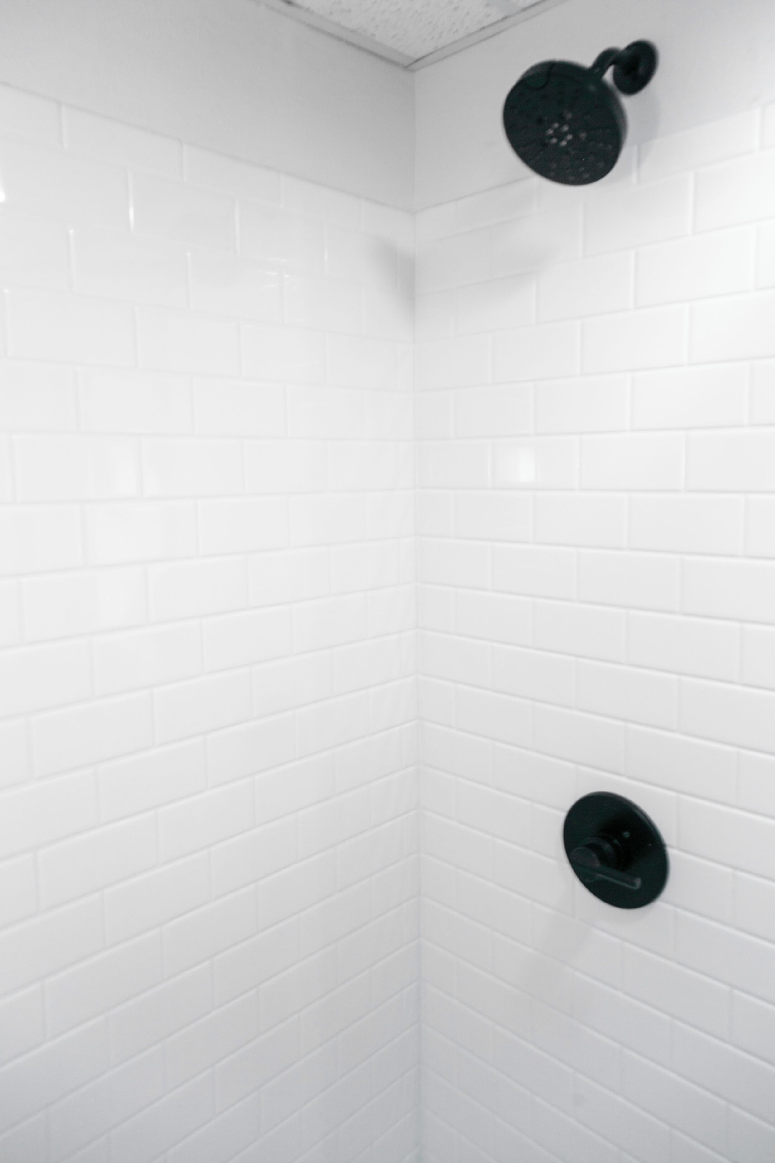 Un coin de pièce aux murs recouverts de carreaux blancs et doté d’une pomme de douche noire.