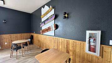 Una habitación con una mesa y sillas de madera, una pared negra decorada con una tabla de snowboard y esquíes, y un extintor.