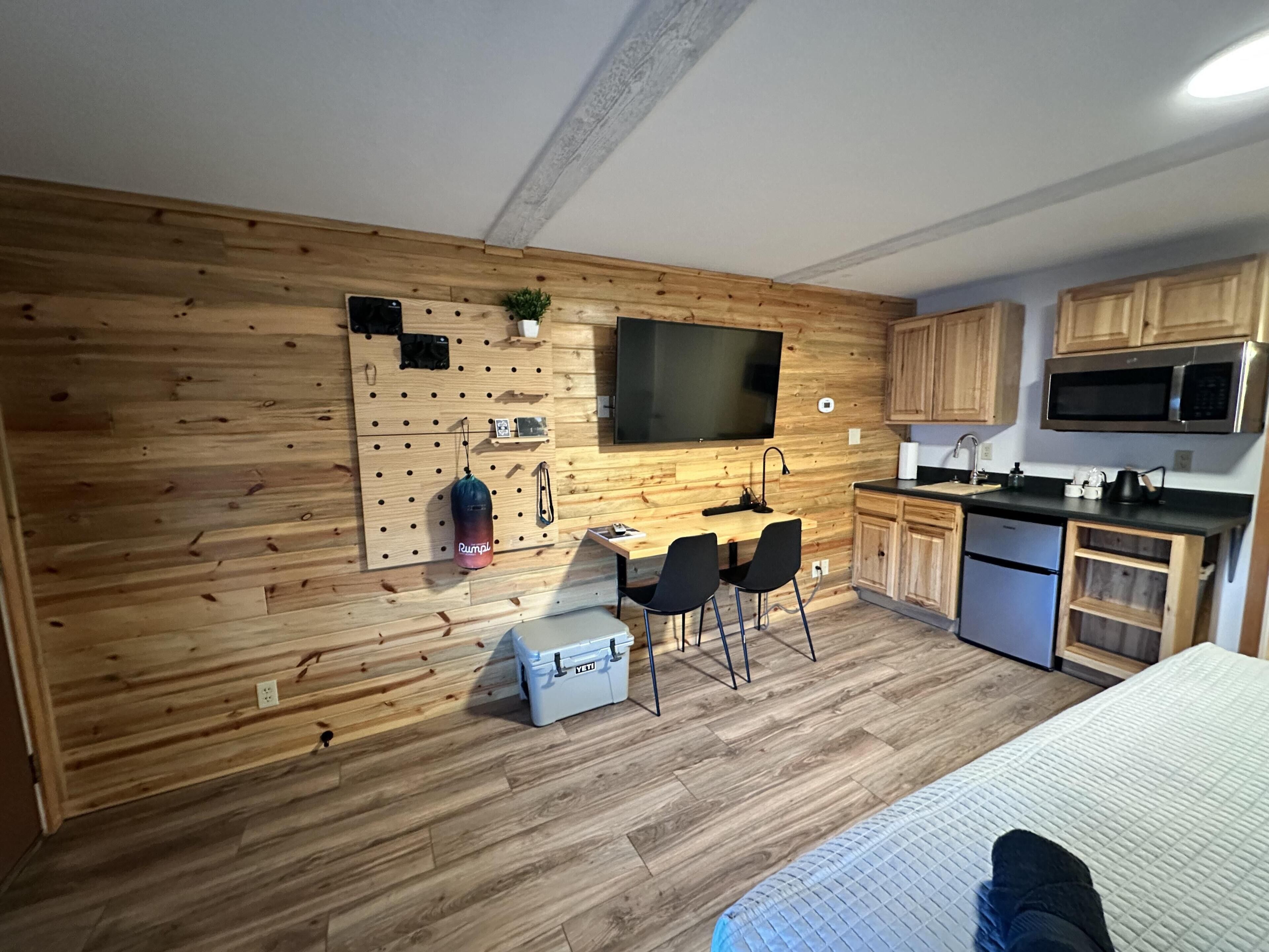 A compact kitchen with wooden walls, a flat-screen TV, a microwave, and a sink.