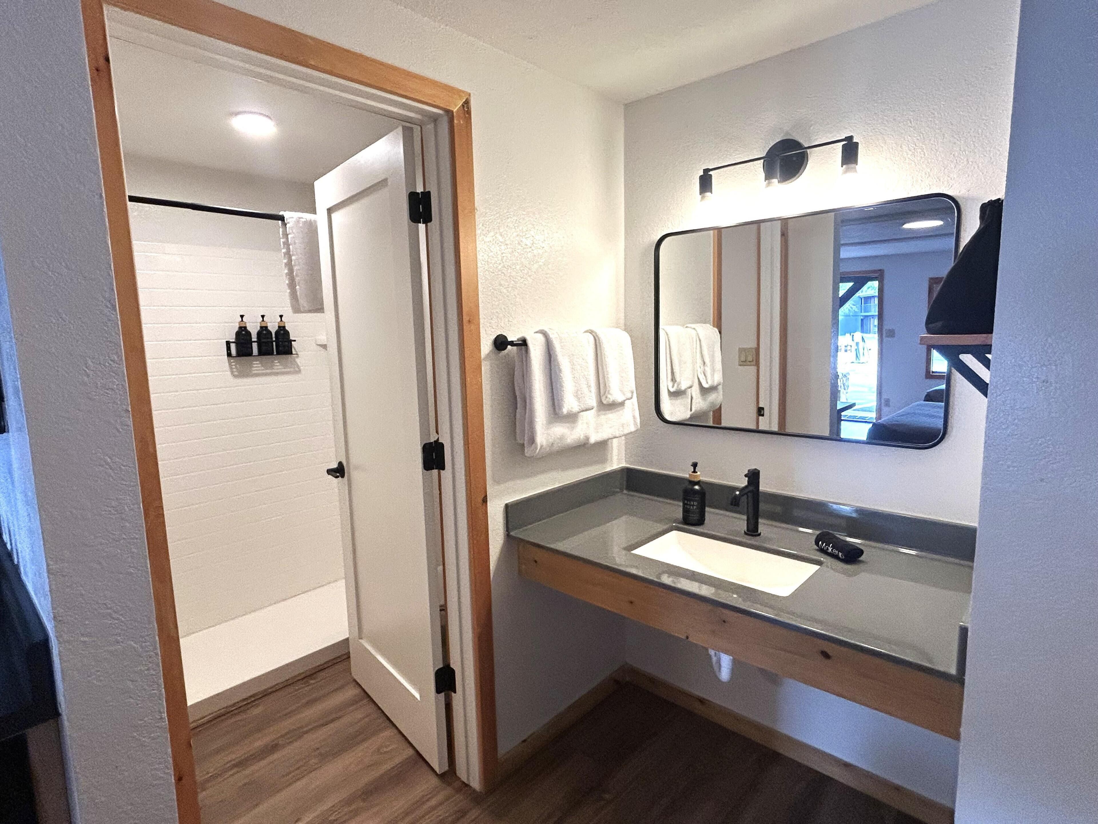 A bathroom with a wooden door, a white sink, a mirror, and a towel rack.