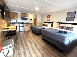 Habitación de hotel compacta con kitchenette, cama con dos almohadas, escritorio con silla y pequeño almacenamiento.