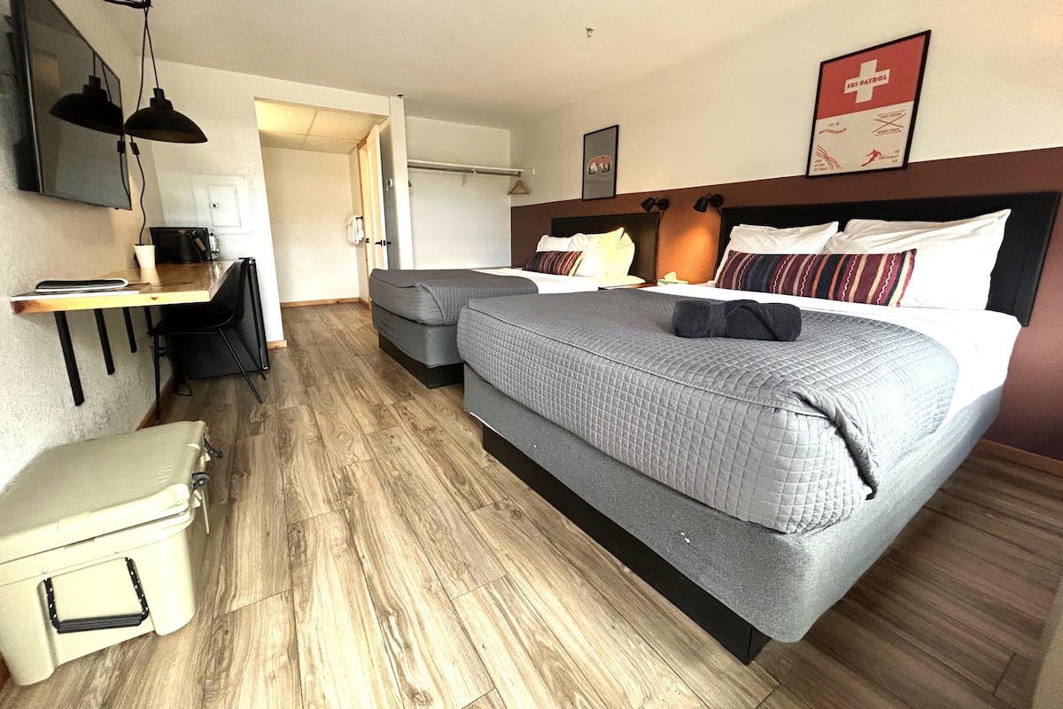 A hotel room with a bed, a desk, a chair, a small table, a coat rack, and a coat storage unit.
