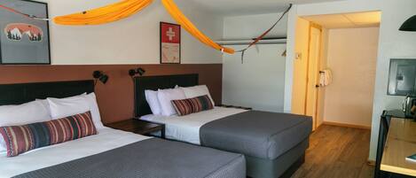 A hotel room with two beds, a wooden floor, a small desk, and a door leading to a bathroom.