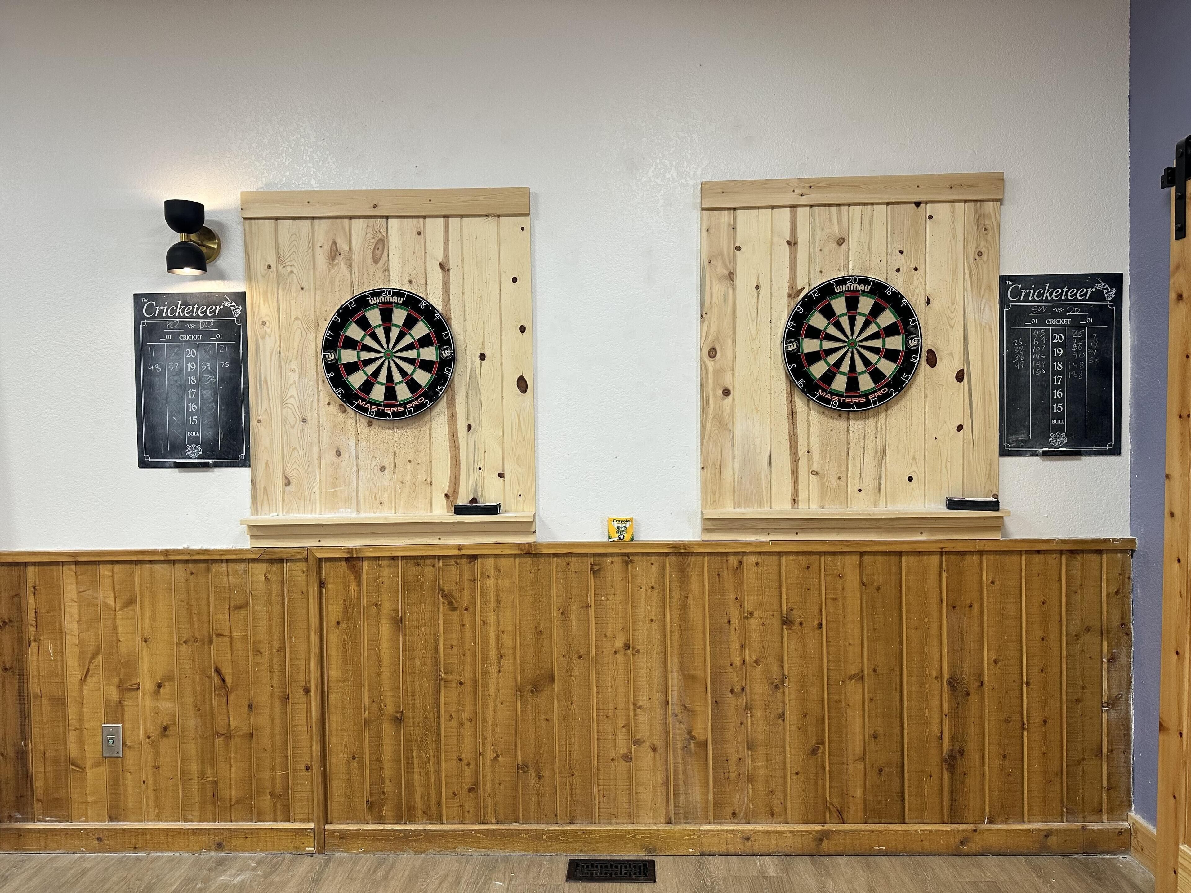 Two dartboards mounted on wooden panels with scoreboards beside them.