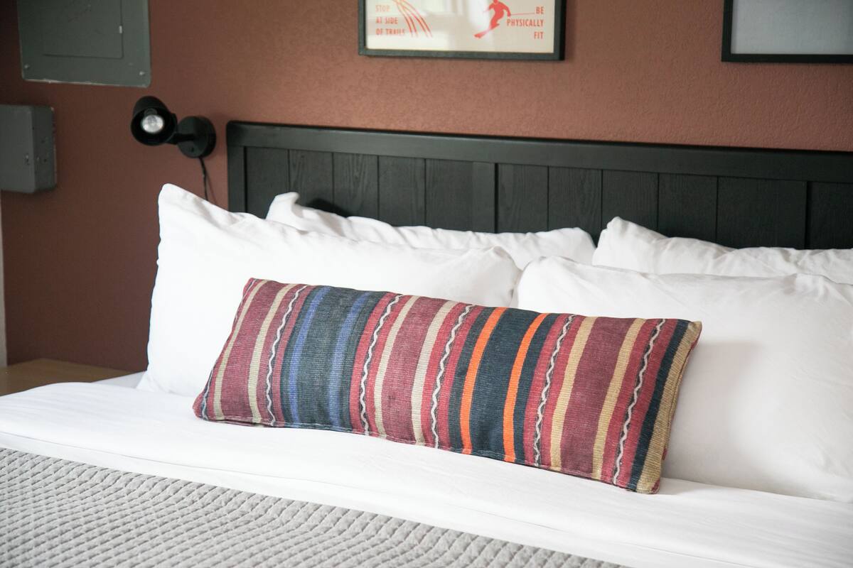 A neatly made bed with white linens and a colorful striped pillow.