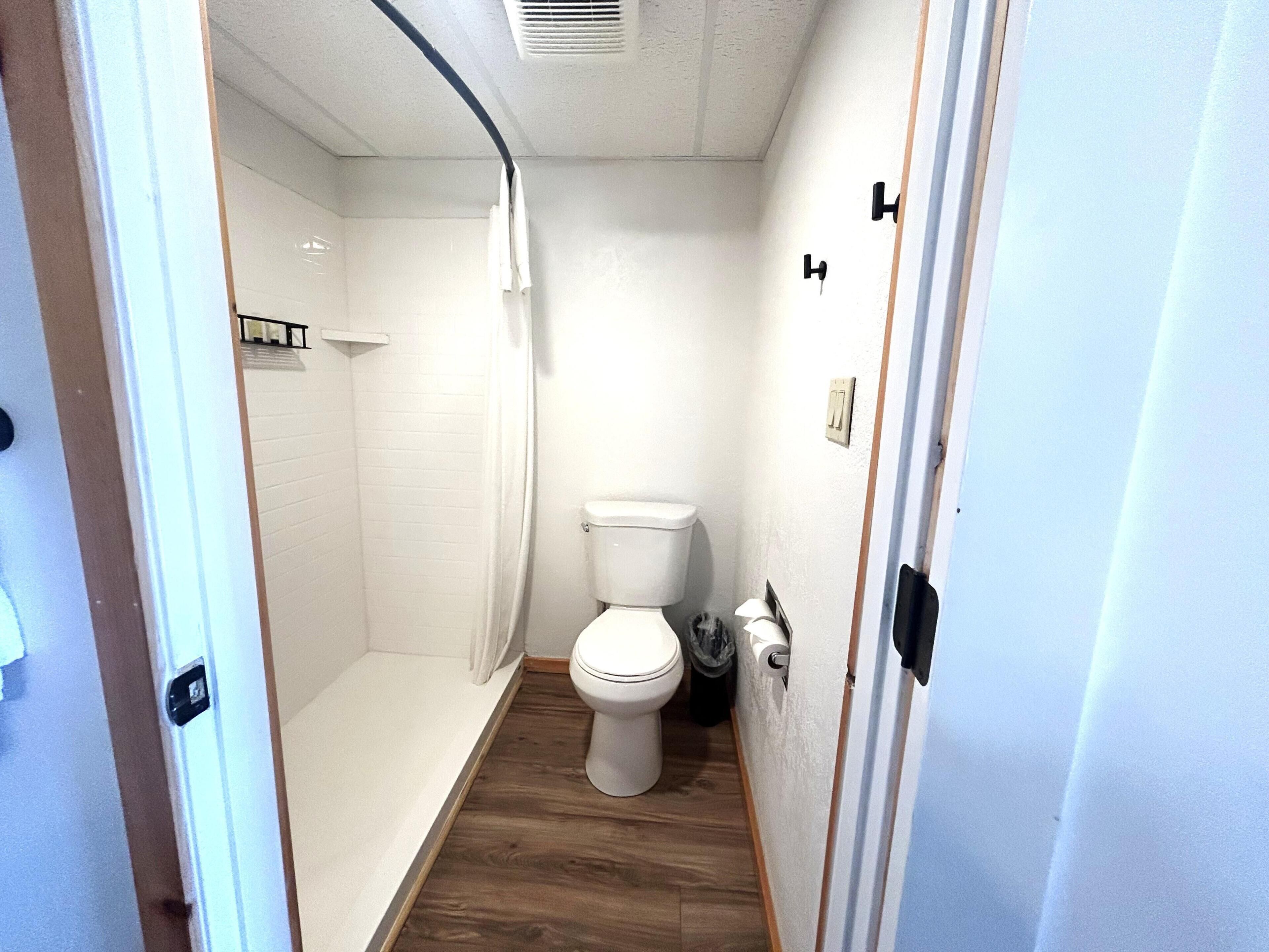 Une petite salle de bain compacte, dotée d’une douche, de toilettes et d’un plancher en bois.