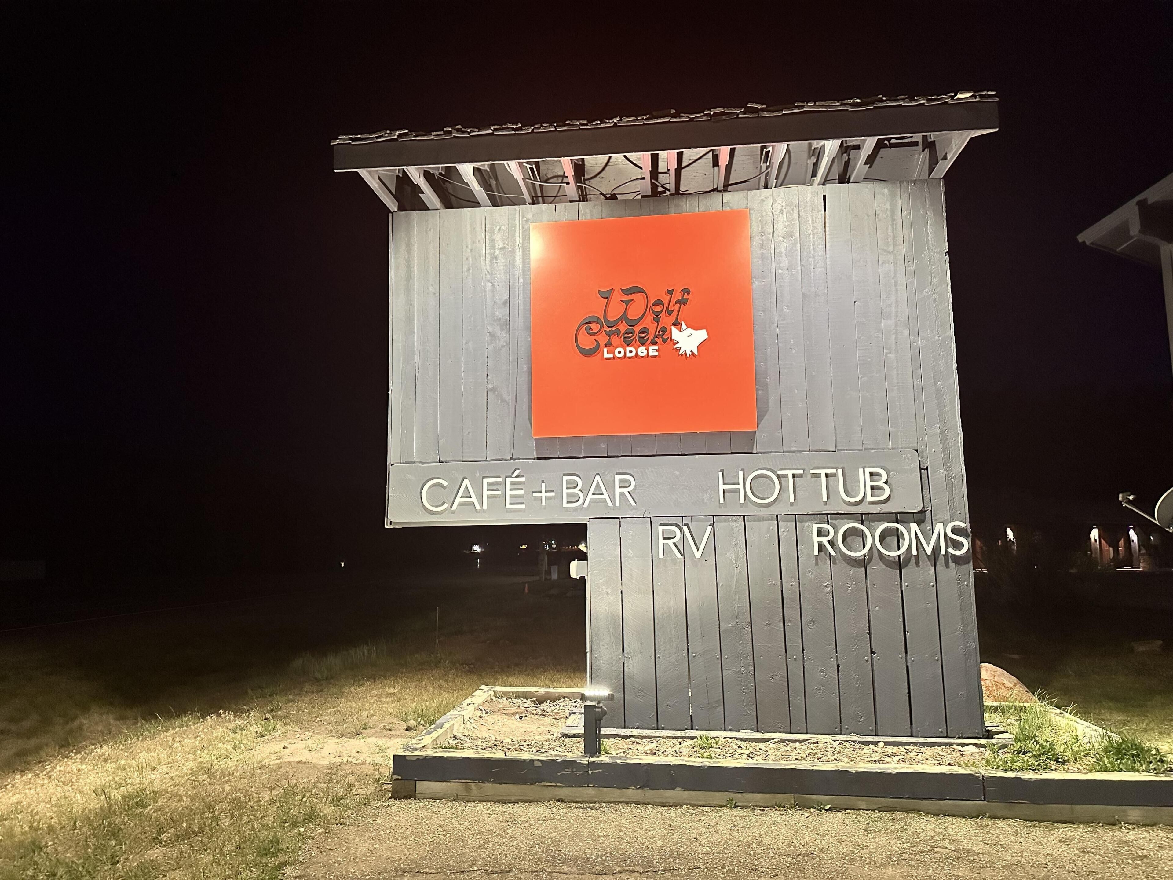 A wooden signboard with 'Wolf Creek Lodge' and amenities listed: café, bar, hot tub, RV, and rooms.