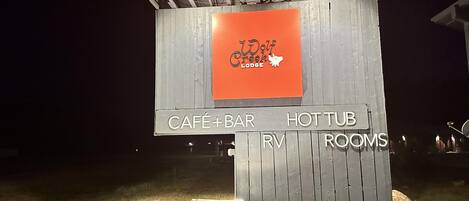 A wooden signboard with 'Wolf Creek Lodge' and amenities listed: café, bar, hot tub, RV, and rooms.