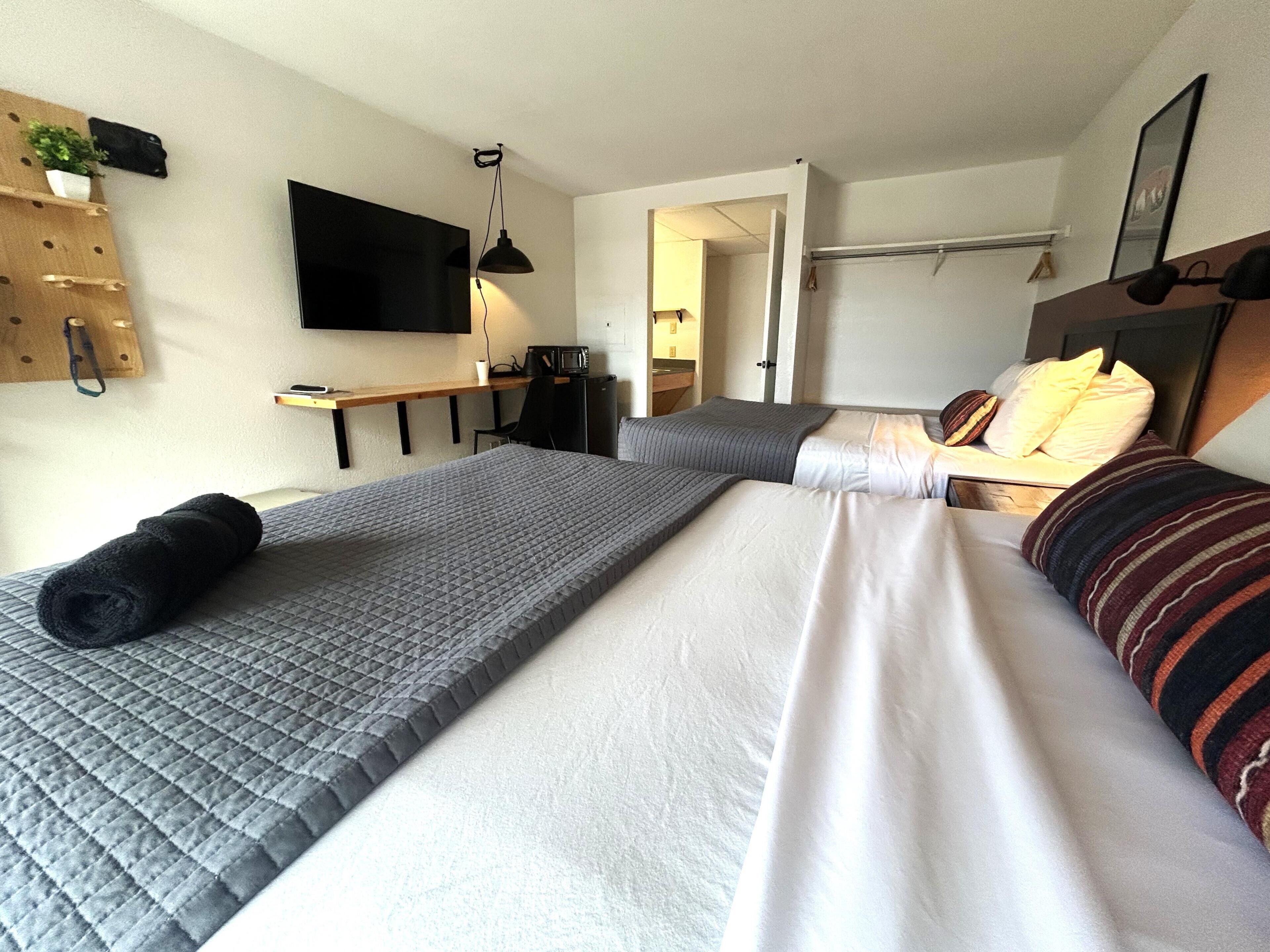 A hotel room with two beds, a desk, a TV, and a microwave.