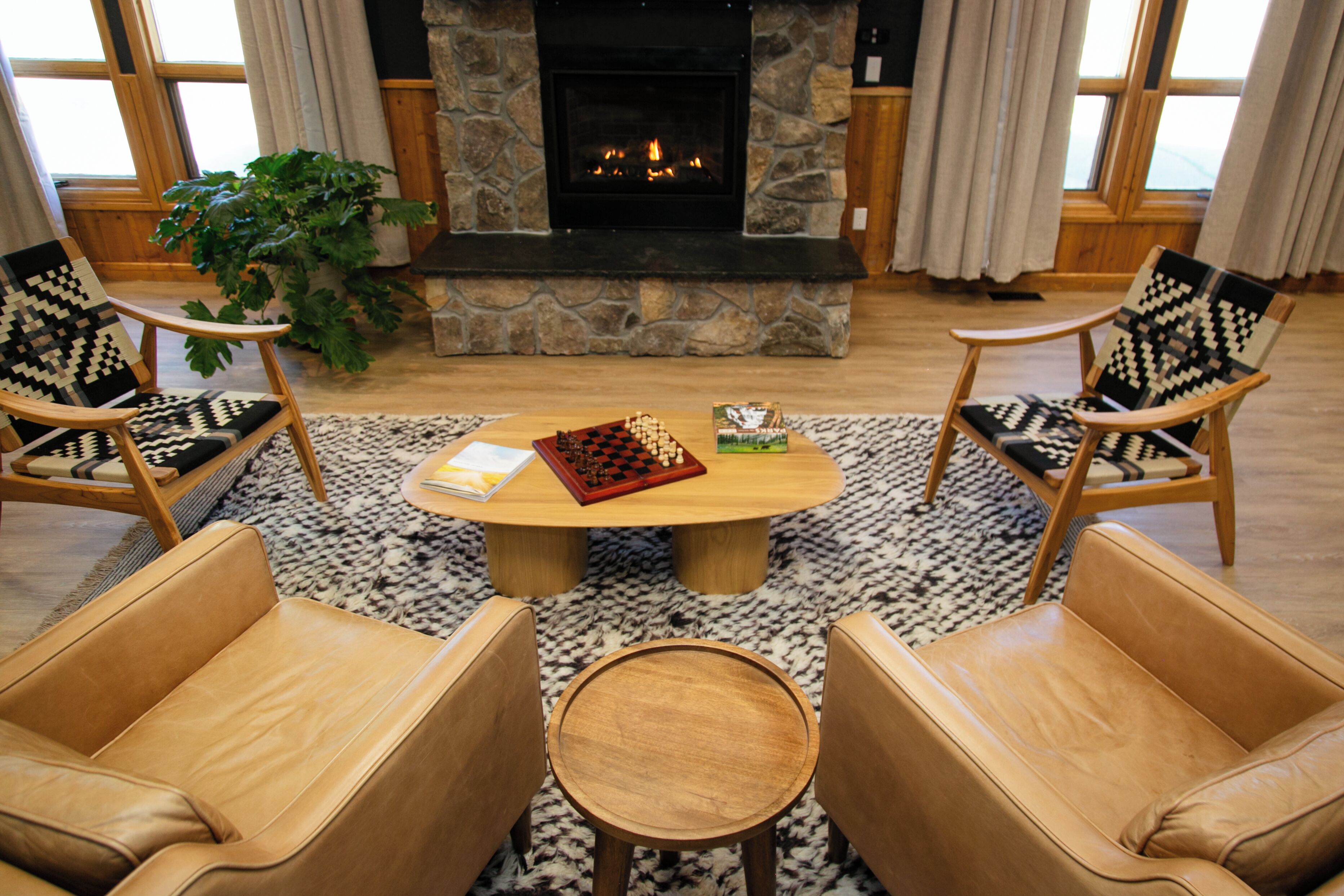 A cozy living room with a fireplace, two leather armchairs, a coffee table, and a potted plant.