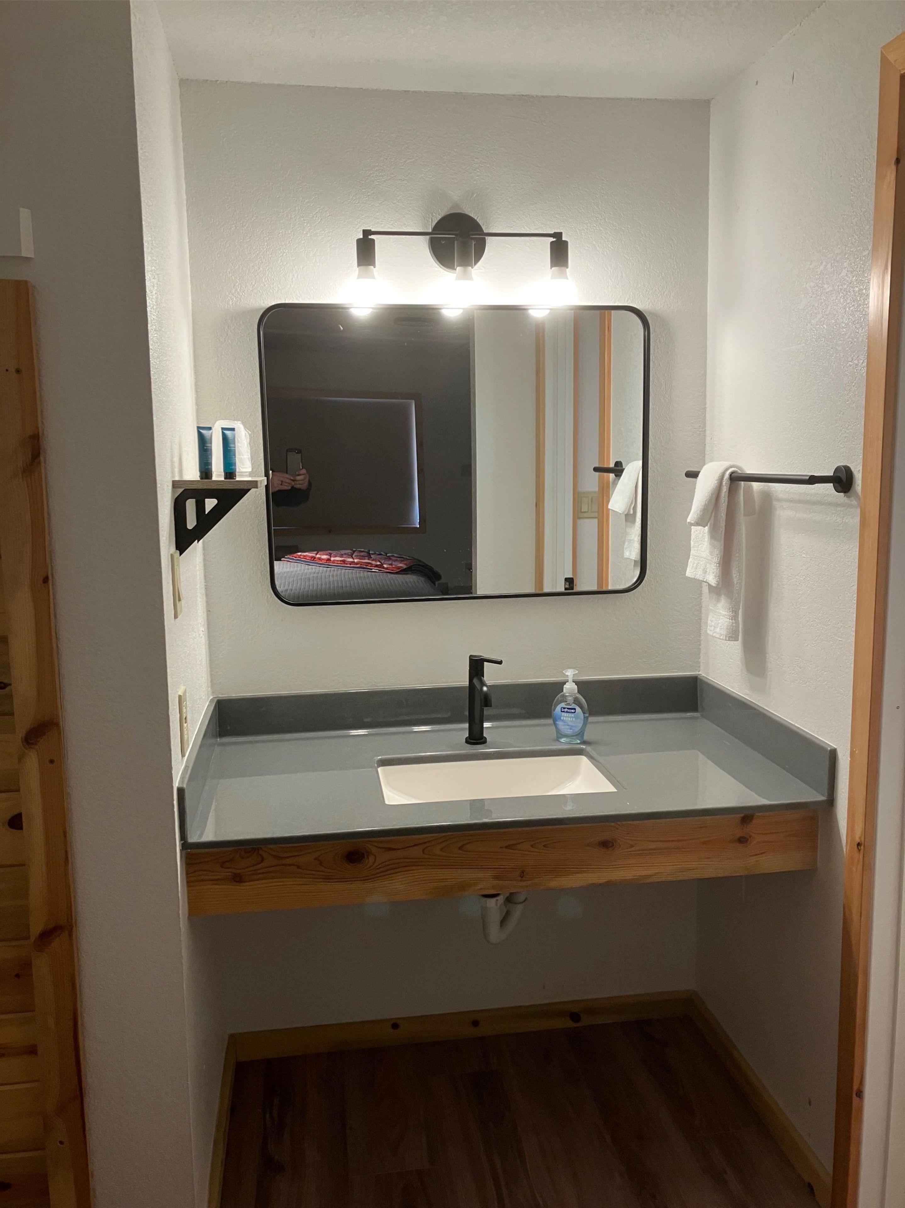 Un baño con espejo, lavamanos, toallero y tocador de madera.