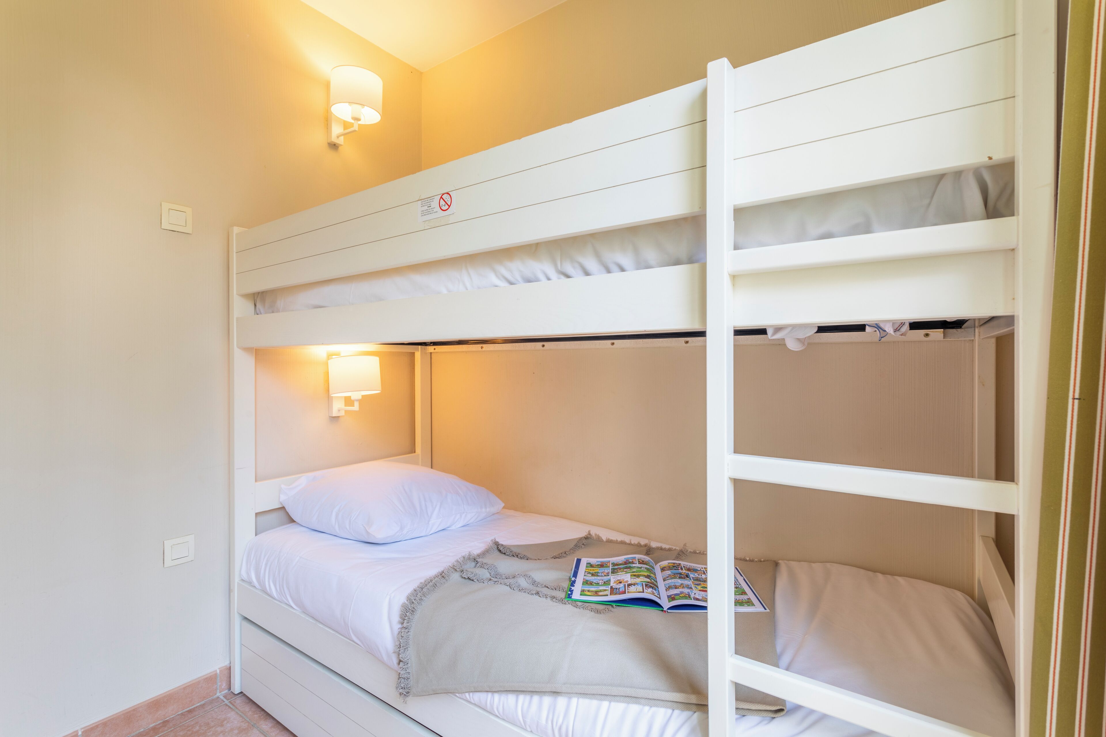 A bunk bed with a light fixture above the top bunk and a book on the lower bunk.