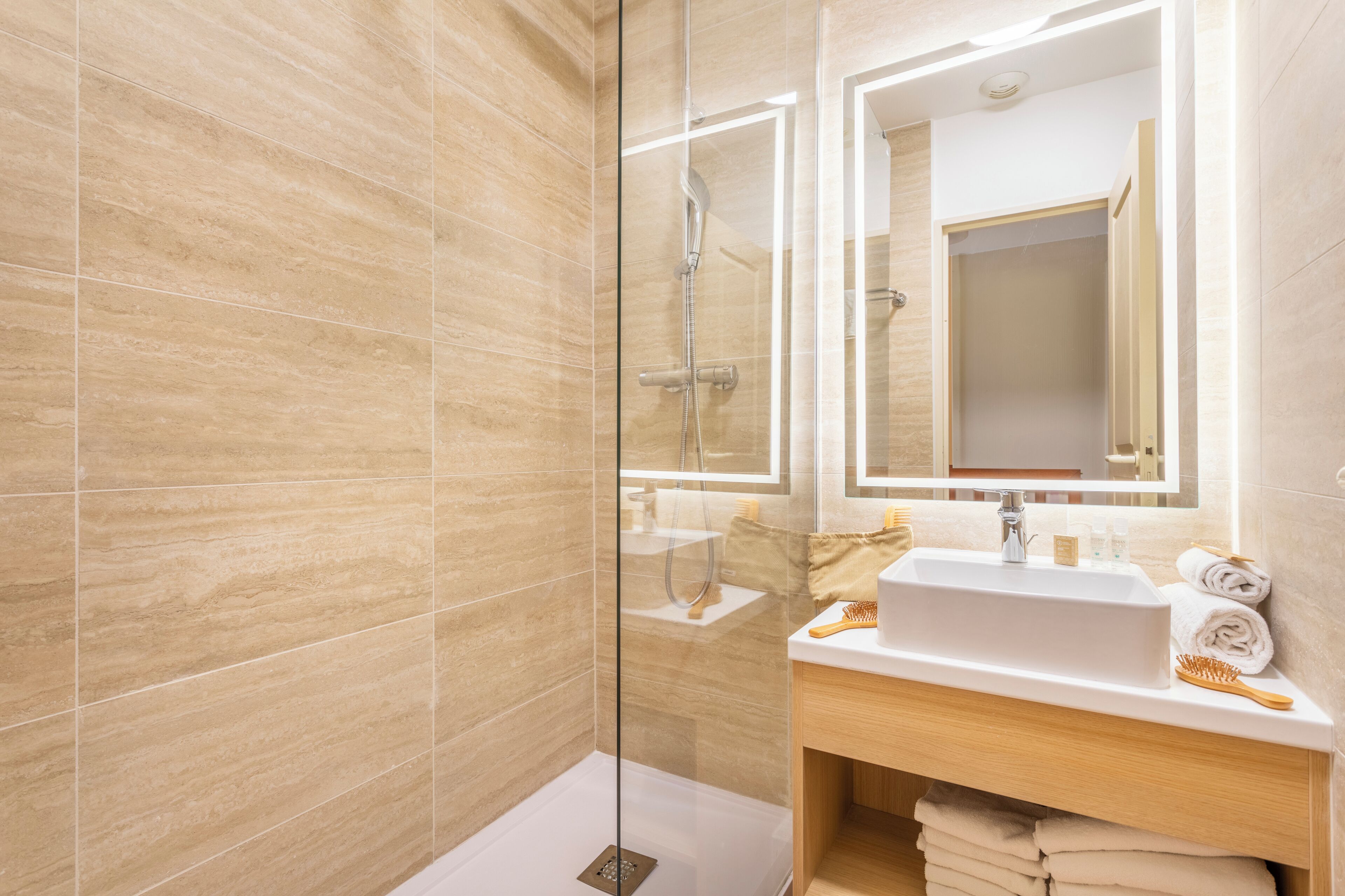 Un baño moderno con ducha envuelta en vidrio, un lavabo blanco y un mueble de tocador de madera.