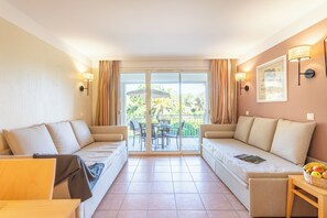 A modern hotel room with a balcony, two sofas, a small table, and a basket of fruit. - Résidence Pierre & Vacances Le Hameau de la Pinède (Hyères)