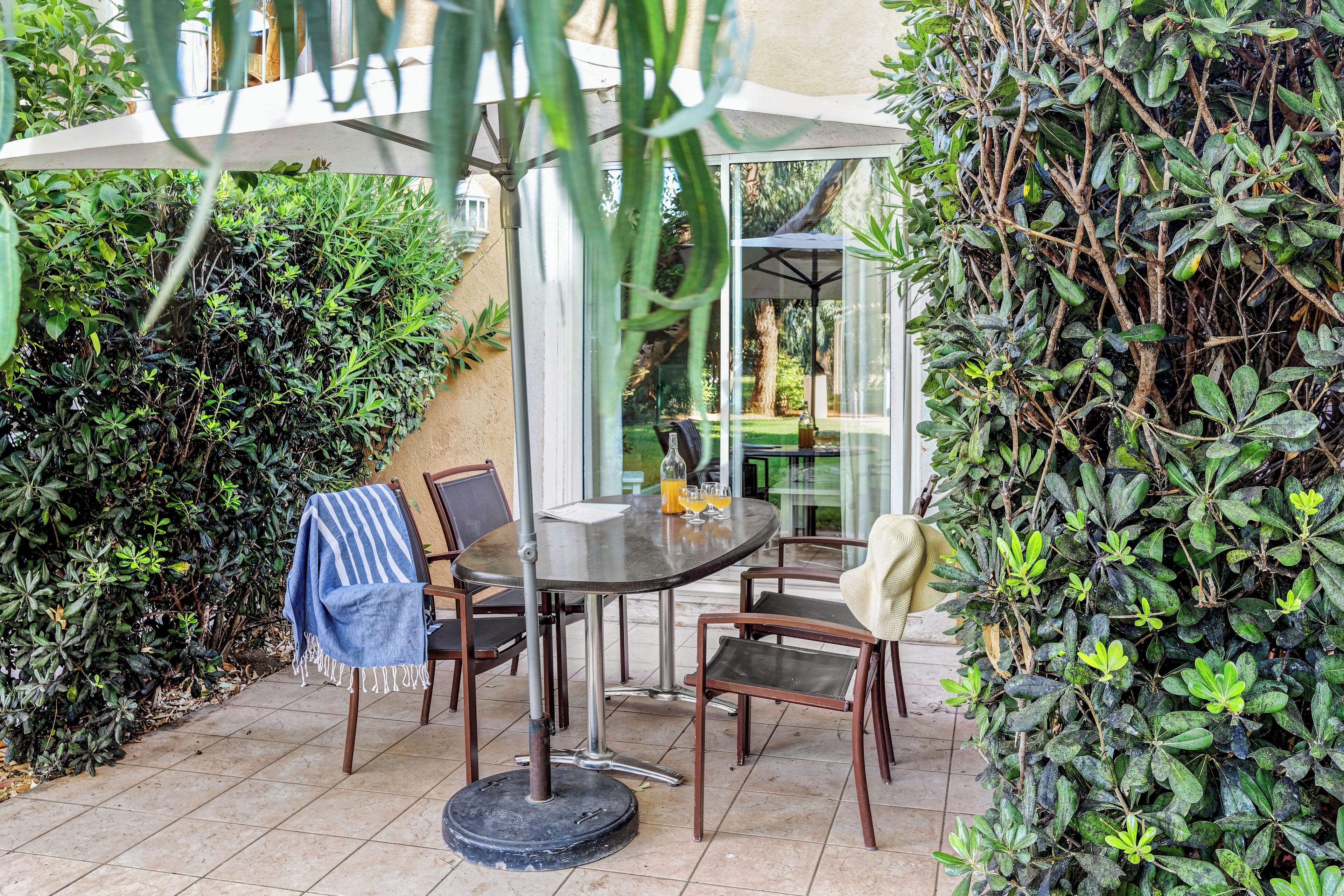 An outdoor patio with a table and chairs, surrounded by dense foliage and a glass enclosure.