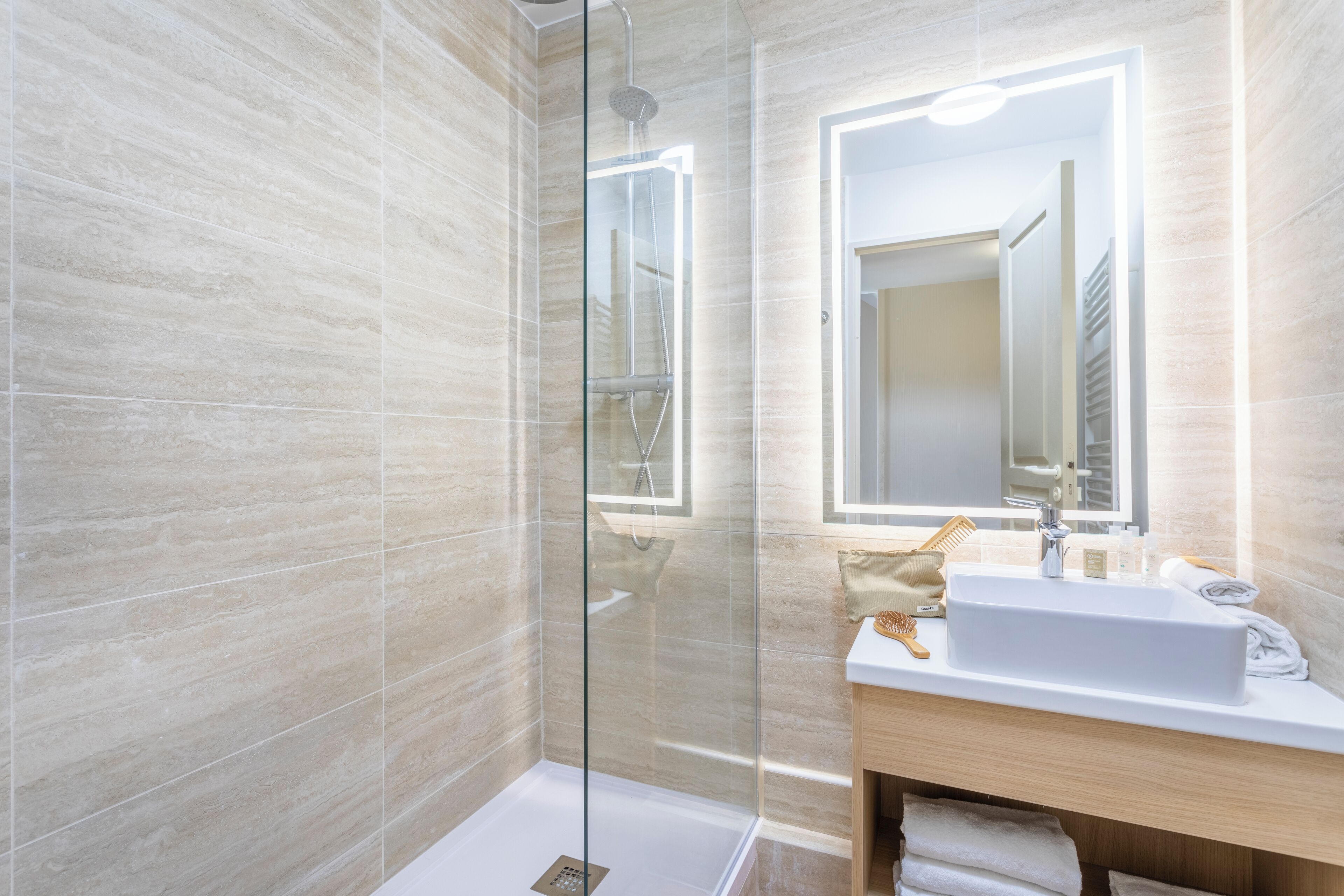 A modern bathroom with a glass-enclosed shower, a white sink, and a mirror with integrated lighting.