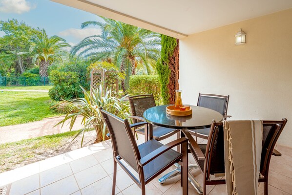 Un comedor con una mesa redonda y sillas, con vista a un jardín con palmeras y un sendero.