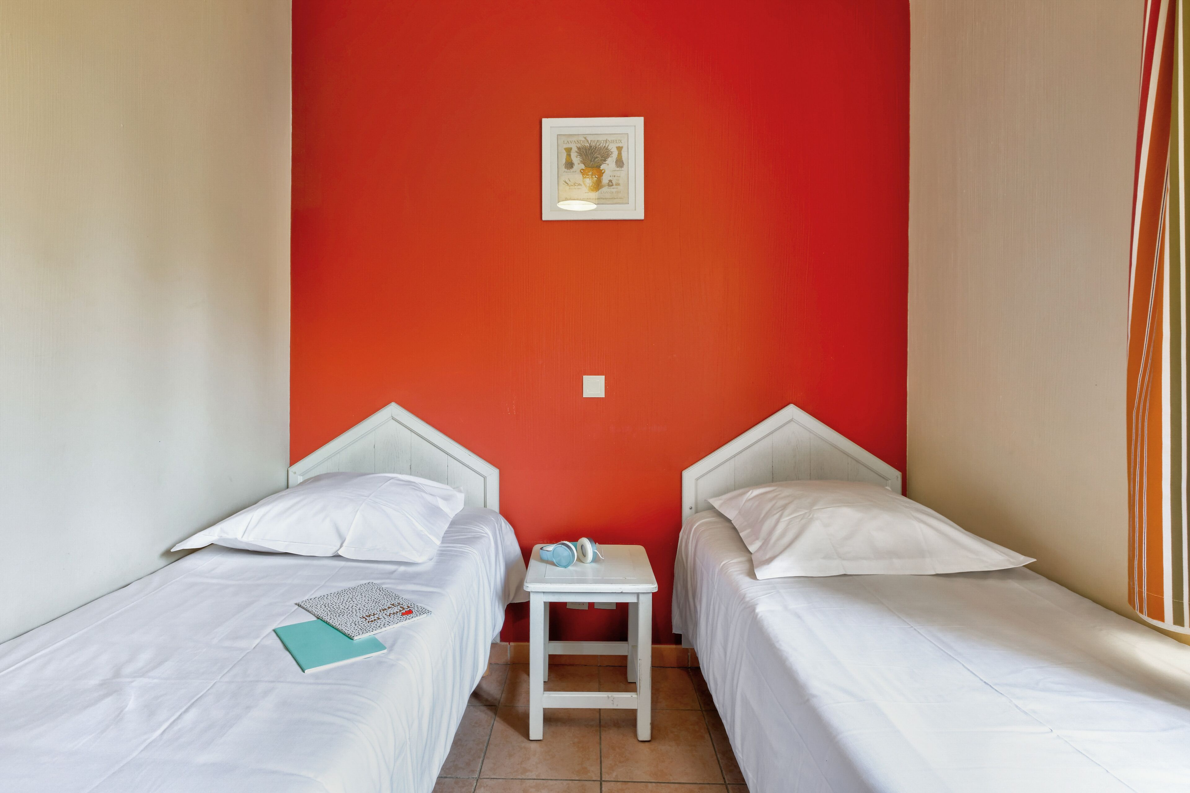 Una habitación pequeña con dos camas, una mesita y un cuadro enmarcado en la pared.