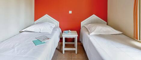 Una habitación pequeña con dos camas, una mesita y un cuadro enmarcado en la pared.