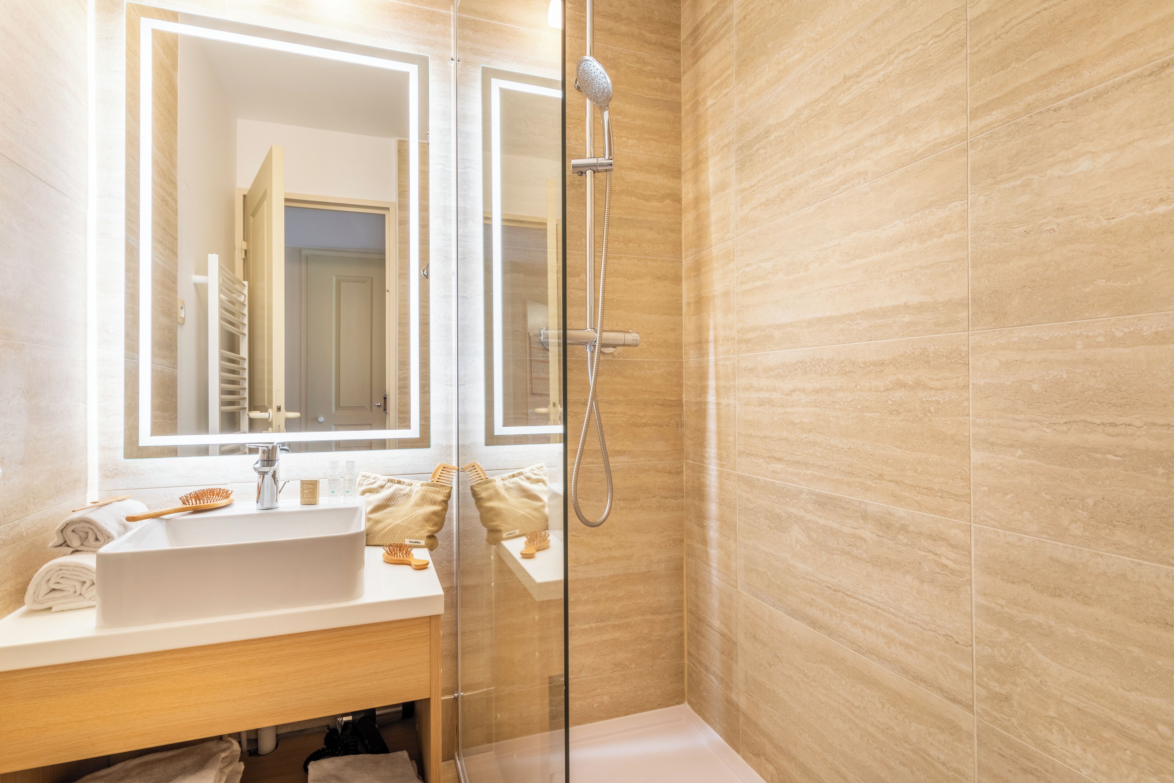 Un baño moderno con cabina de ducha de vidrio, un espejo grande y un lavabo blanco con artículos de aseo.