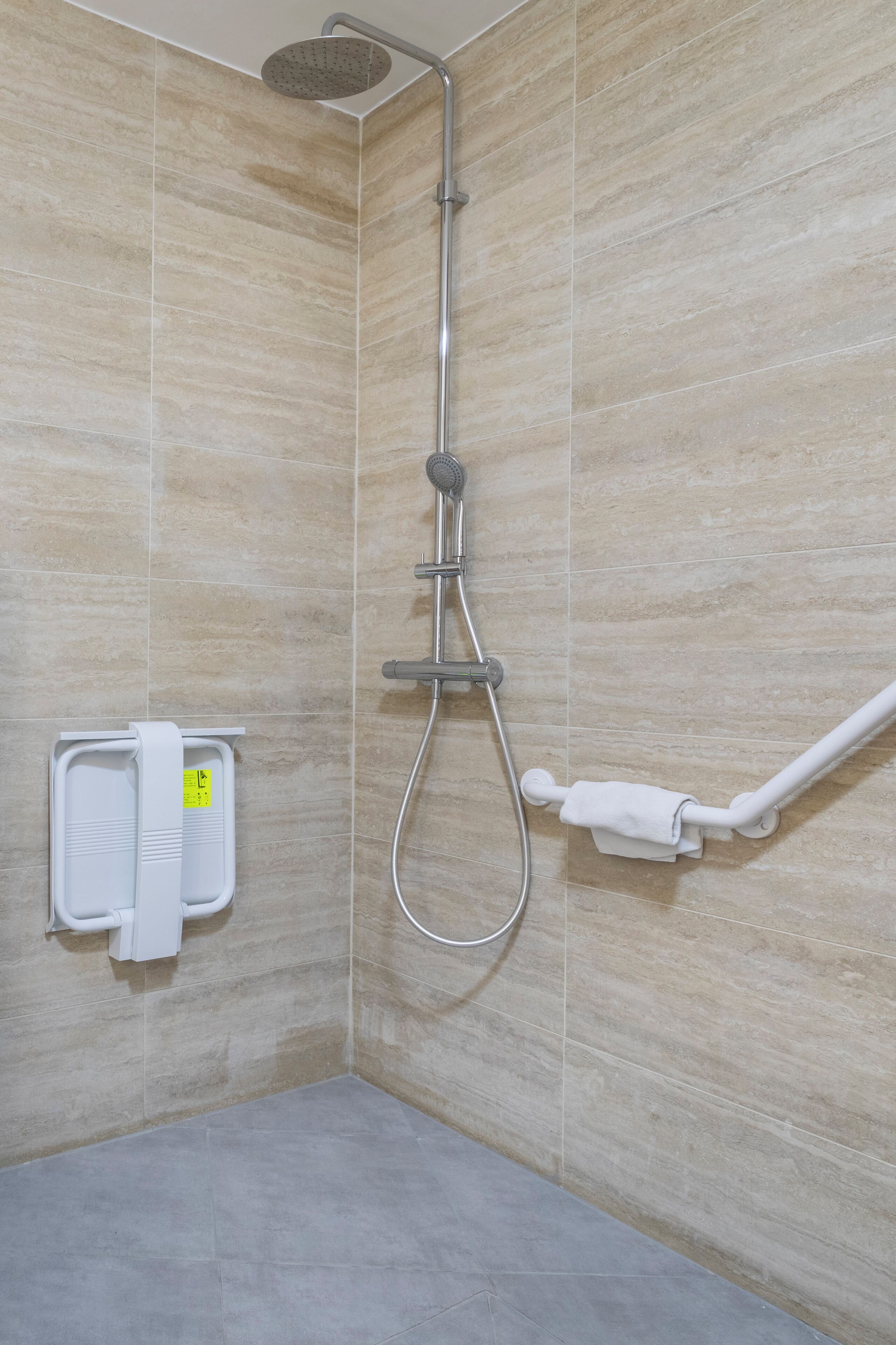 A shower area with a handheld showerhead, a wall-mounted towel rack, and a white grab bar.