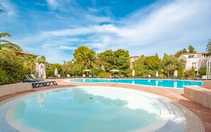 Una gran piscina al aire libre rodeada de sillones de descanso y sombrillas, con árboles y edificios al fondo.