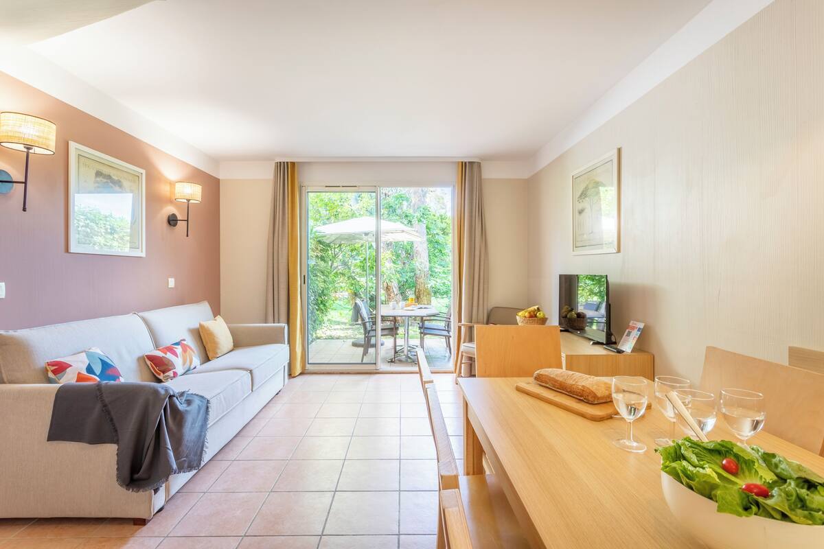 A modern living room with a sofa, a dining table with a salad bowl, and a TV on a wooden stand.