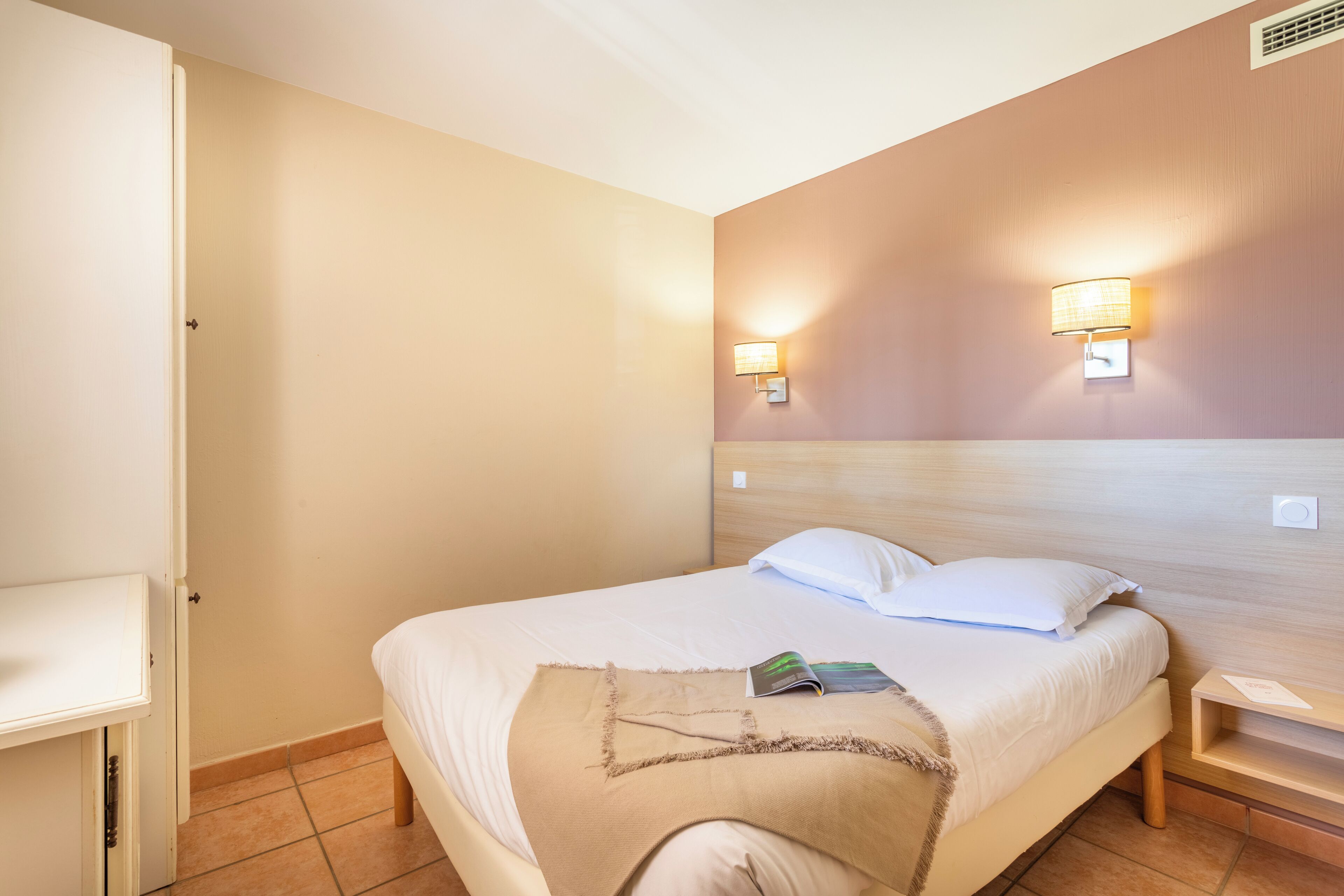 A hotel room with a bed, bedside tables, and wall-mounted lamps.