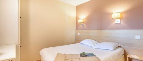 A hotel room with a bed, bedside tables, and wall-mounted lamps.