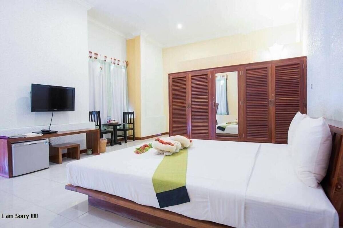 A hotel room with a bed, a desk with a television, a wardrobe, and a small table with chairs.