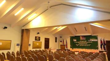 Un salón de conferencias con filas de sillas, un atril y un escenario con banderas.