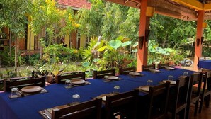 A covered outdoor dining area with tables set for guests, surrounded by lush greenery and a traditional building in the background. - Memoria Palace & Resort (Pailin)