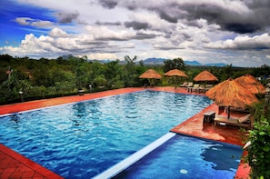 A swimming pool with a red border, surrounded by lounge chairs and thatched umbrellas, with mountains in the background. - Memoria Palace & Resort (Pailin)