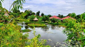 A serene pond surrounded by lush greenery and traditional thatched-roof huts. - Memoria Palace & Resort (Pailin)