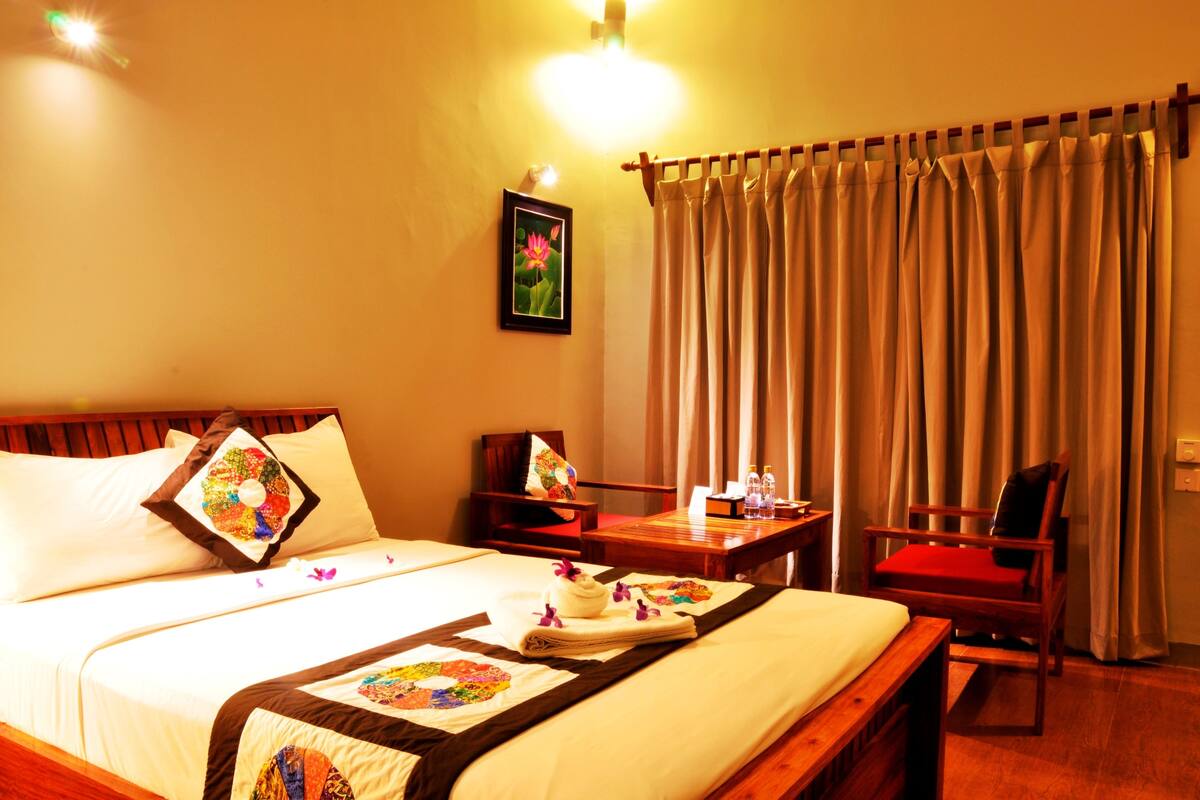 A hotel room with a large bed, two chairs, a small table, and a window with curtains.
